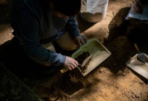 Mackenzee Souers uses a dustpan to remove loose dirt from the dig site.